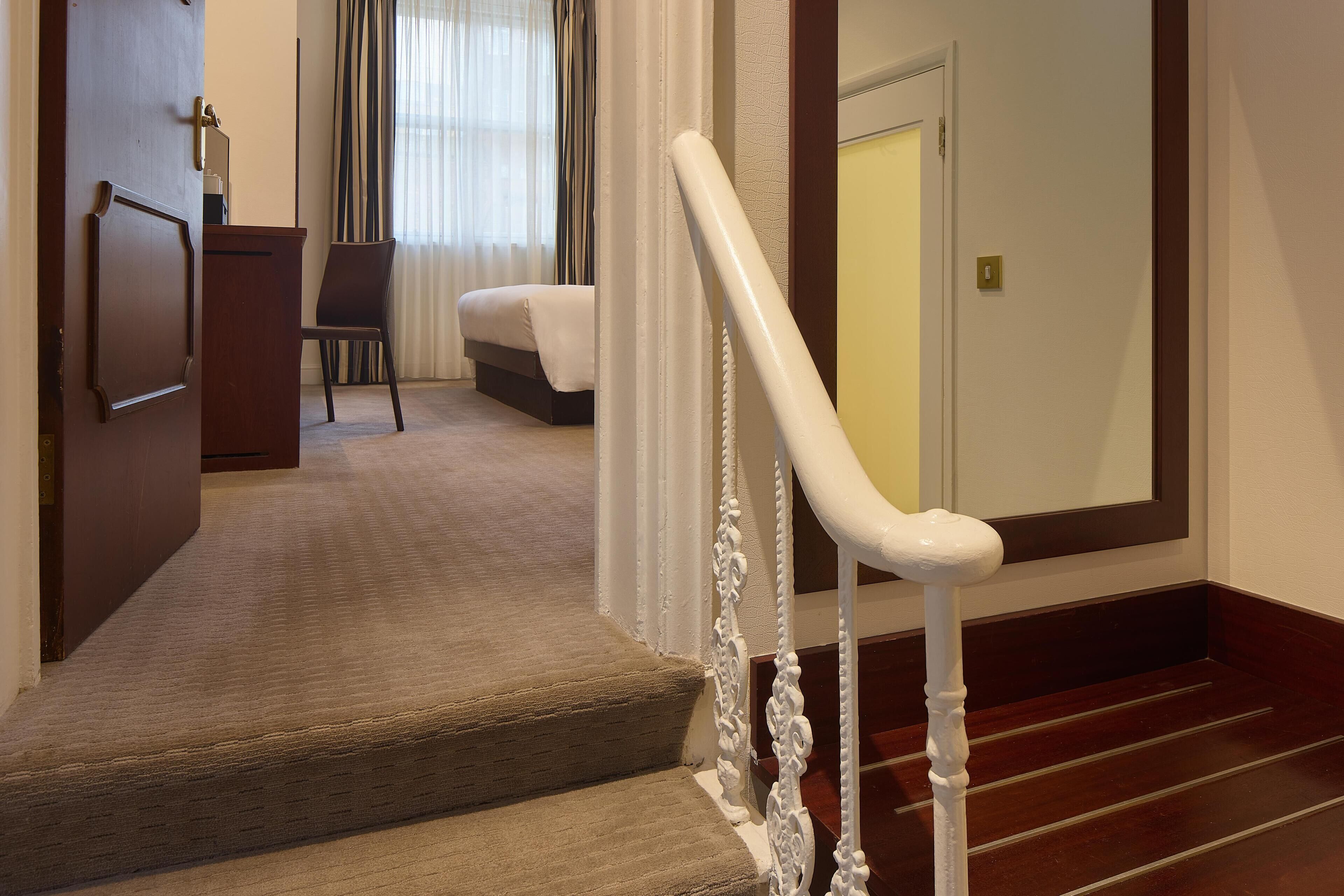 Un escalier avec une rampe blanche mène à une chambre qui contient un lit et une chaise.