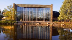 Een modern gebouw met een spiegelende glazen gevel, een stenen basis en een plat dak.