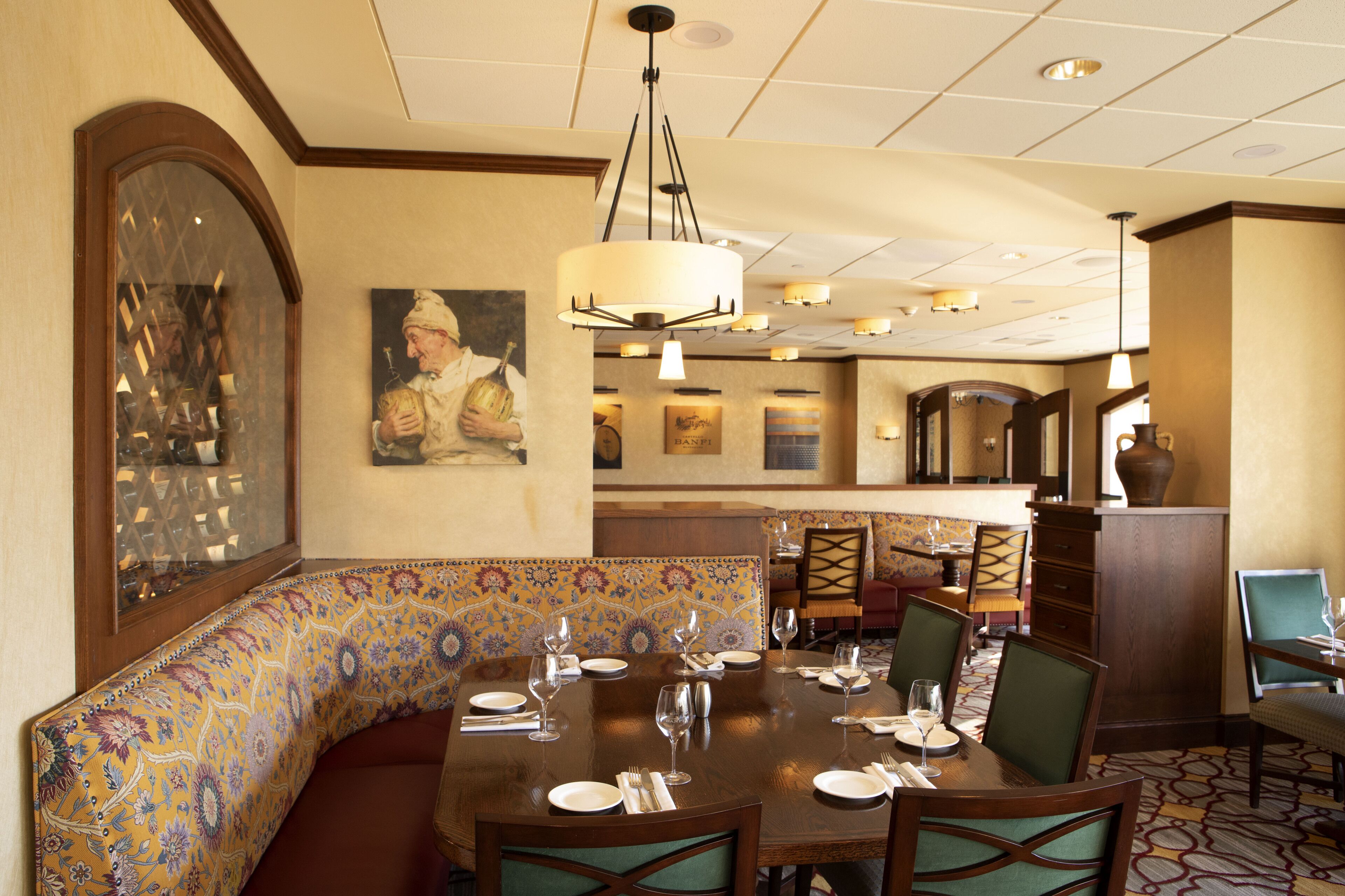 A dining area with a large table set for a meal, a patterned bench, and a painting on the wall.