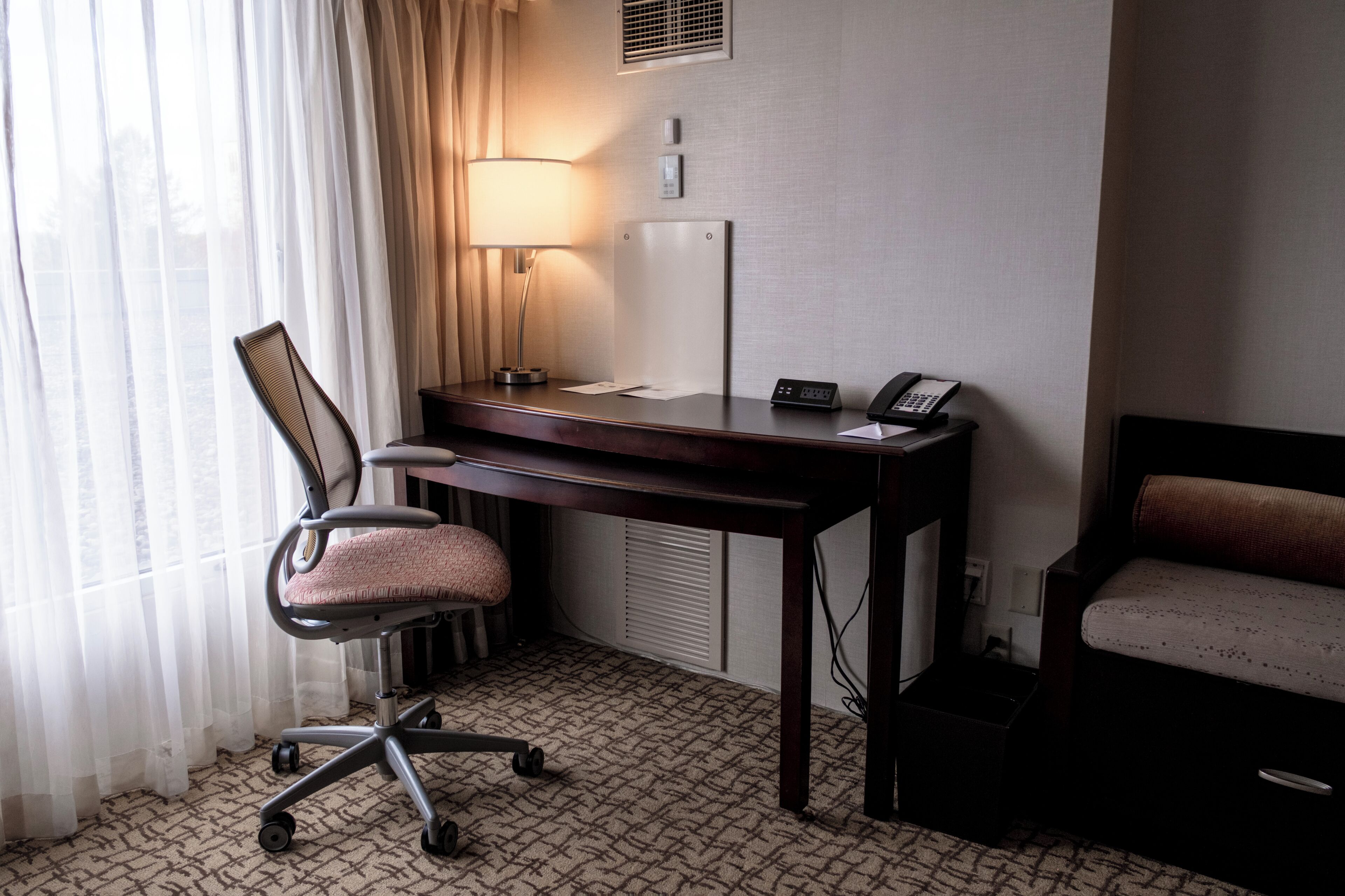 Habitació d'hotel amb escriptori, cadira, làmpada, telèfon i llit.
