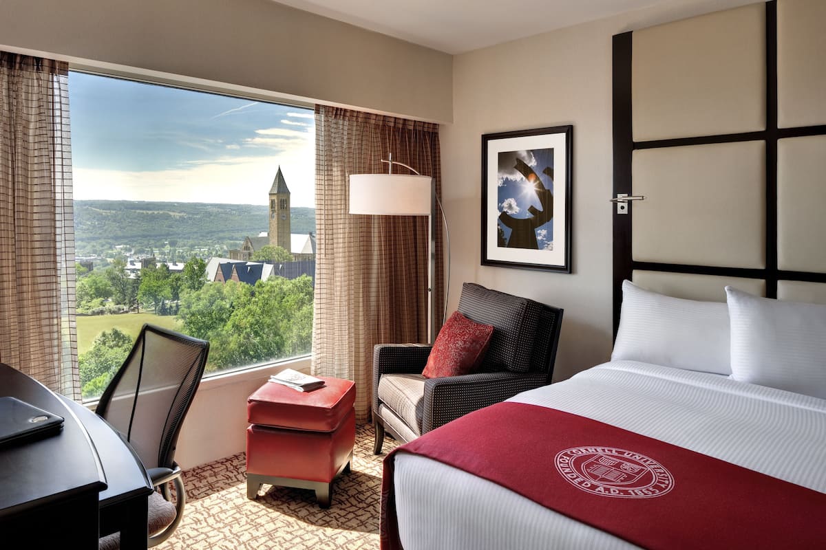 A hotel room with a large window, a bed, a desk, and a chair.