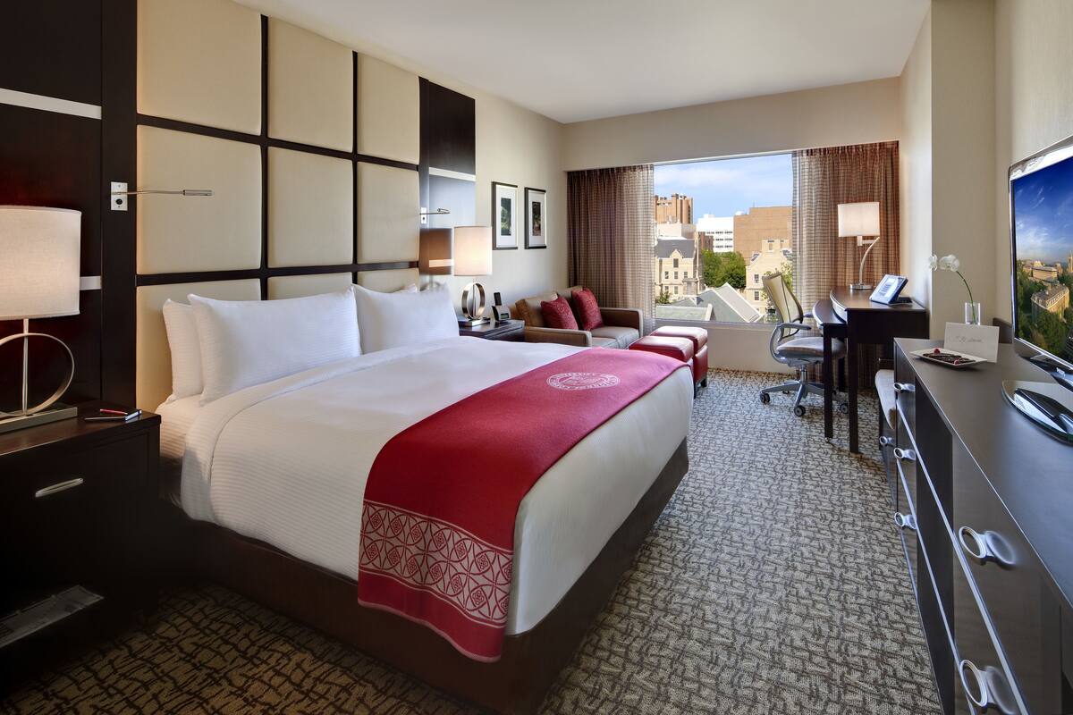 A hotel room with a large bed, a desk, a chair, and a television.