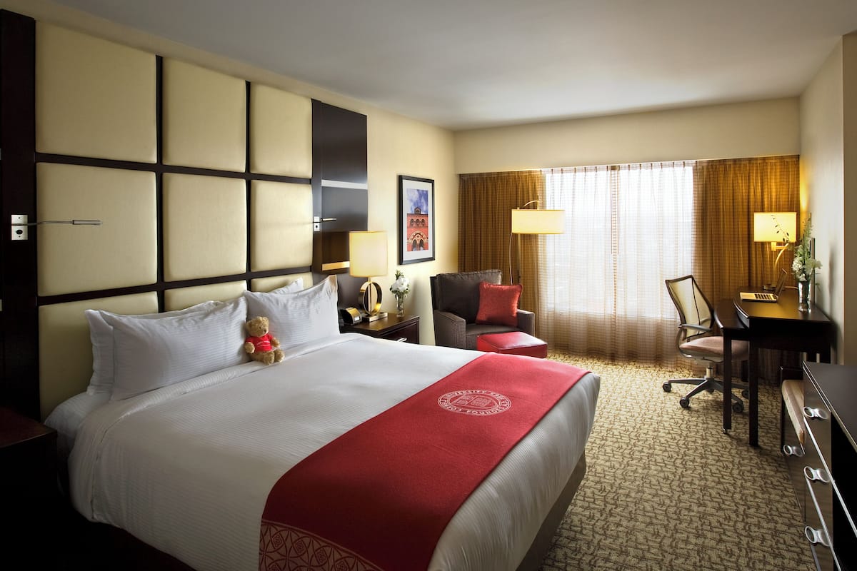 A hotel room with a large bed, a desk, a chair, a desk lamp, and a window with curtains.
