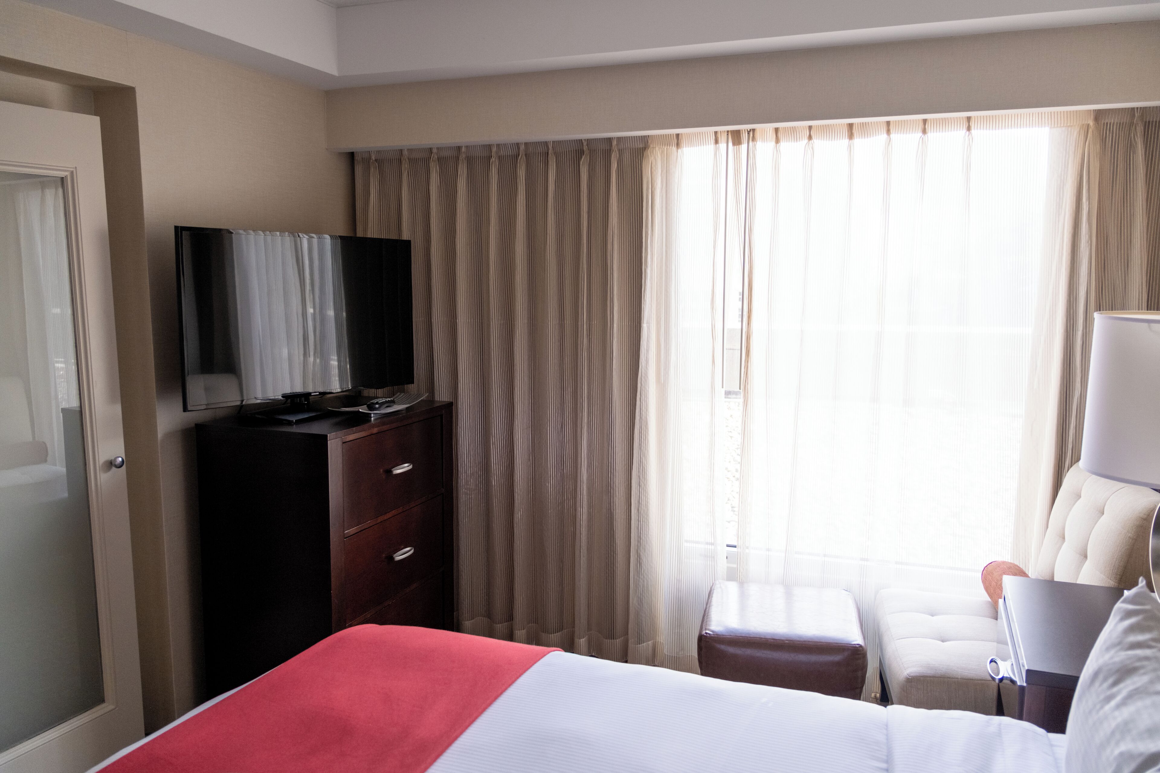 Habitación de hotel con cama, televisor en una cómoda, una silla y ventana con cortinas.