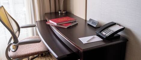 A hotel room with a desk, a telephone, a lamp, and a chair.