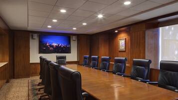 A conference room with a long wooden table, black leather chairs, a large screen, and a framed picture on the wall.