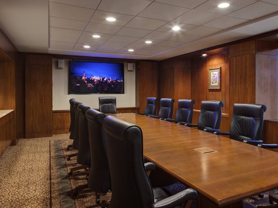A conference room with a long wooden table, black leather chairs, a large screen, and a framed picture on the wall.