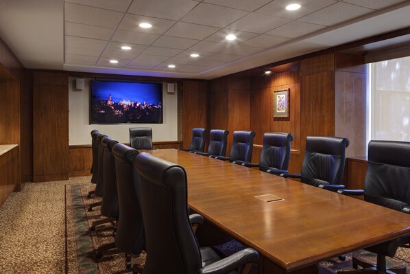 Une salle de conférence avec une longue table en bois, des chaises en cuir noir, un grand écran et un tableau encadré au mur.