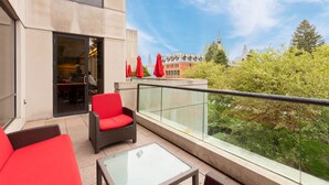 Een balkon met rieten meubels, een glazen tafel en rode parasols.