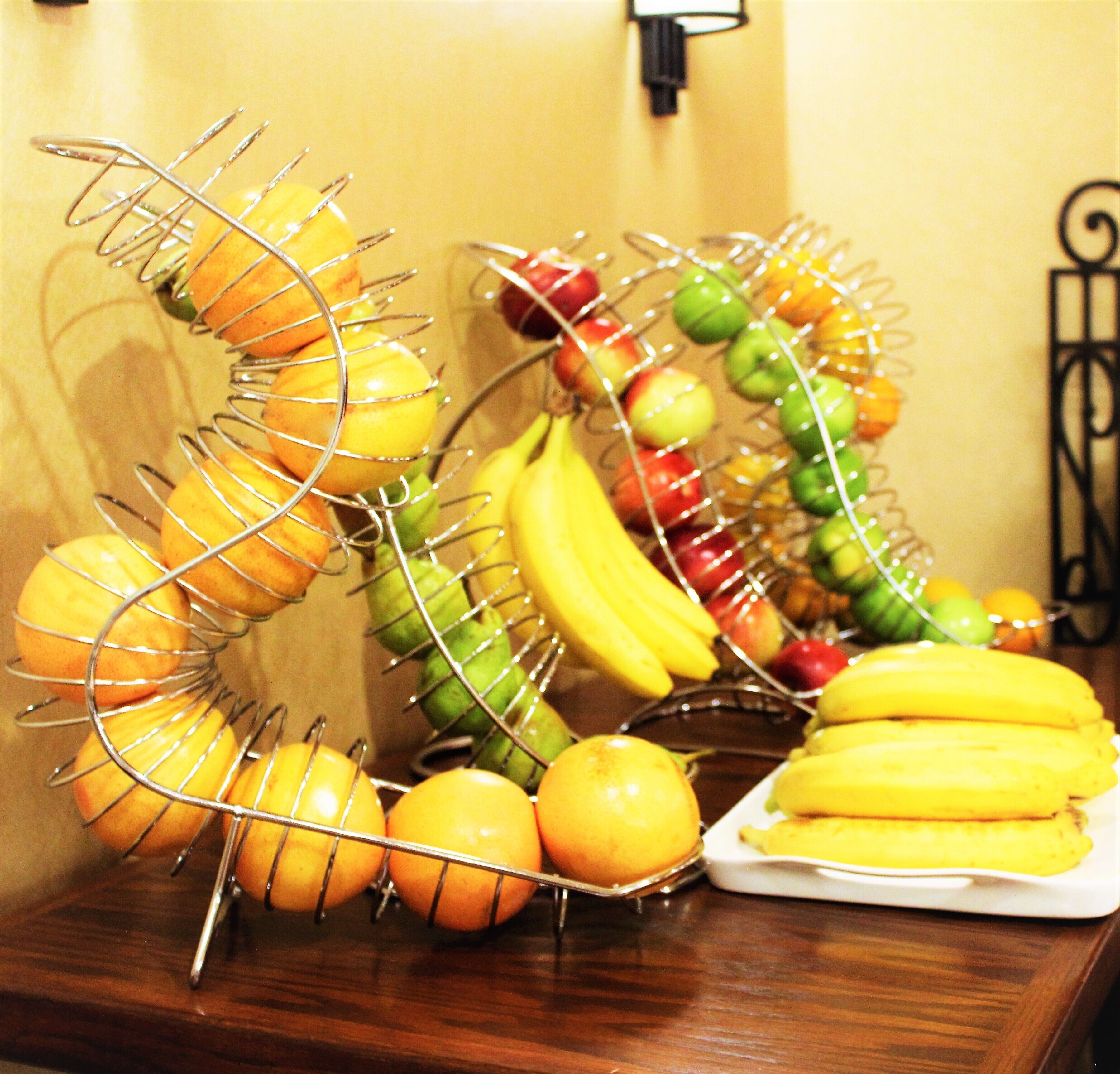 A fruit stand with oranges, bananas, and apples arranged on a wire rack.
