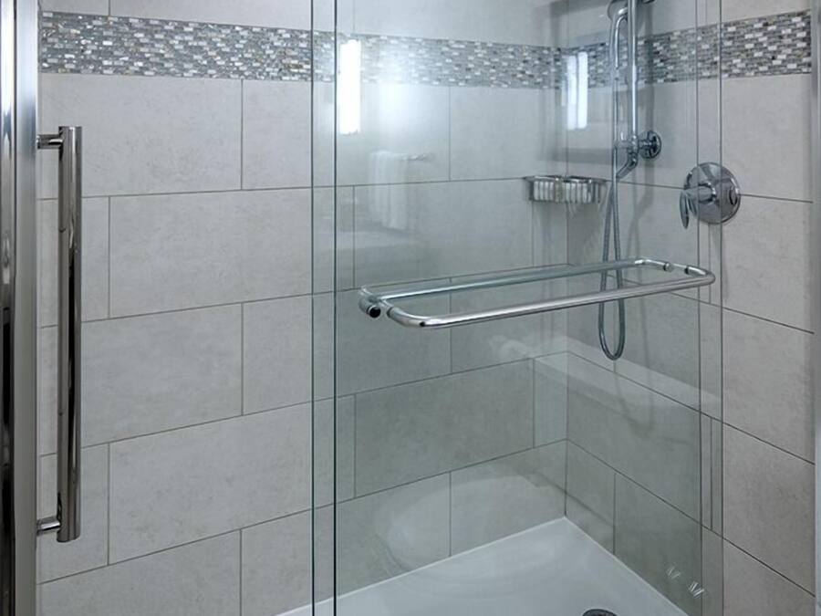 A glass-enclosed shower with a handheld showerhead, a handheld showerhead, and a glass-enclosed bathtub.