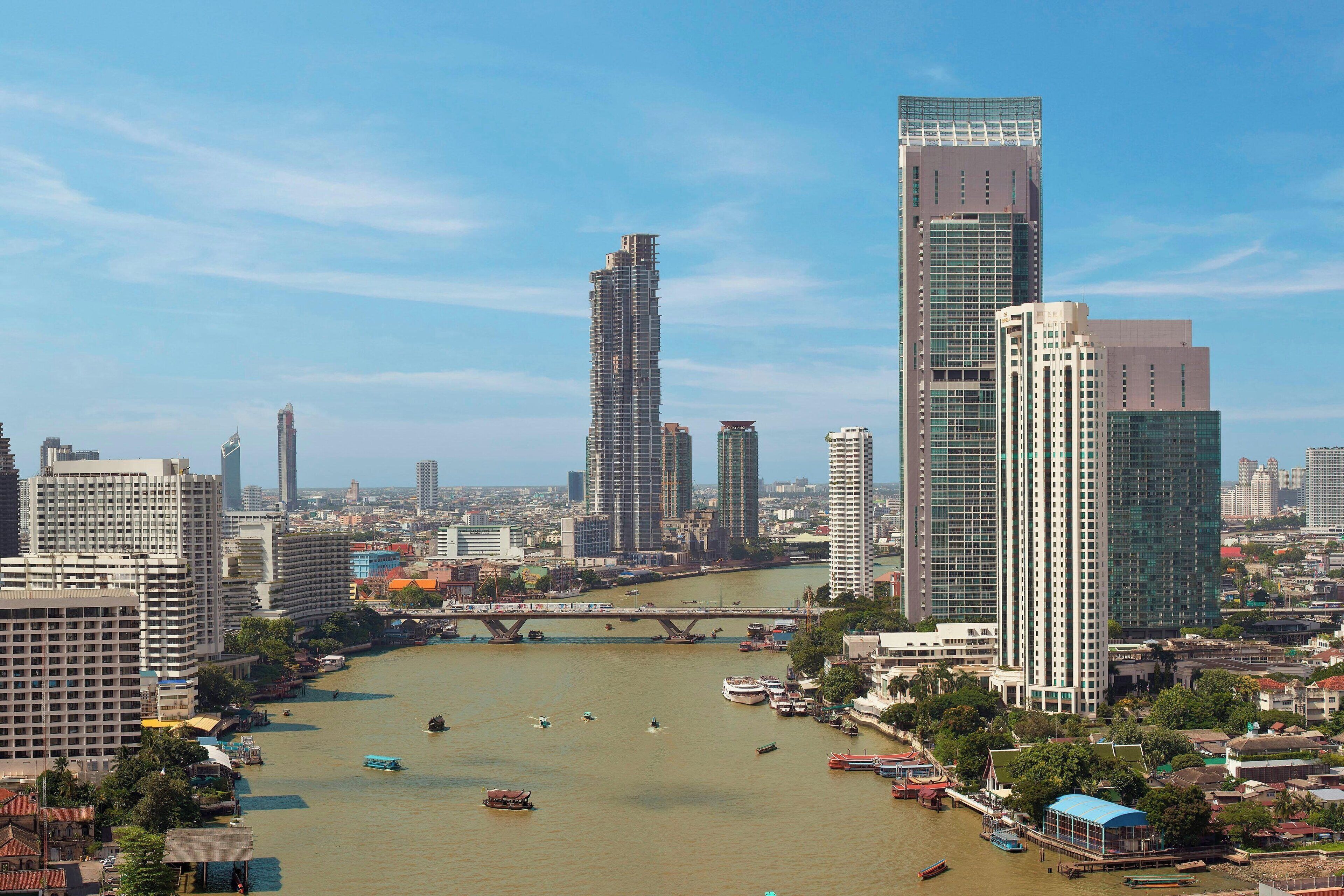 A cityscape with modern high-rise buildings, a river with boats, and a bridge.