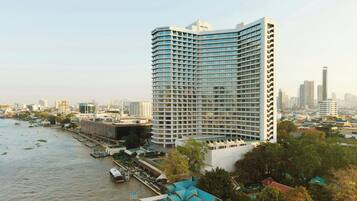 A high-rise hotel with a curved facade, located near a river with a dock and boats.
