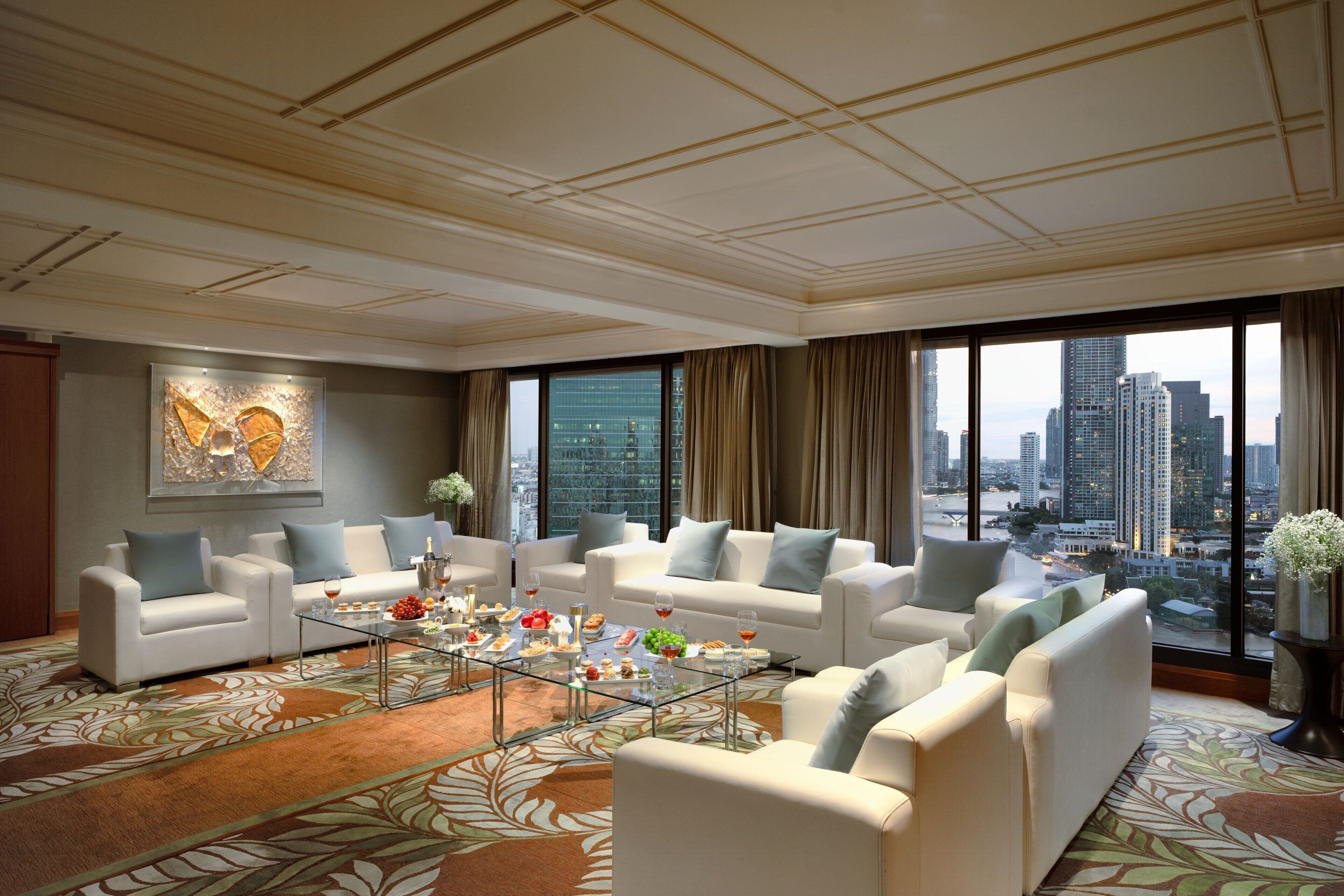 A spacious living room with a city view, featuring a large sofa set, a glass coffee table, and a decorative wall piece.