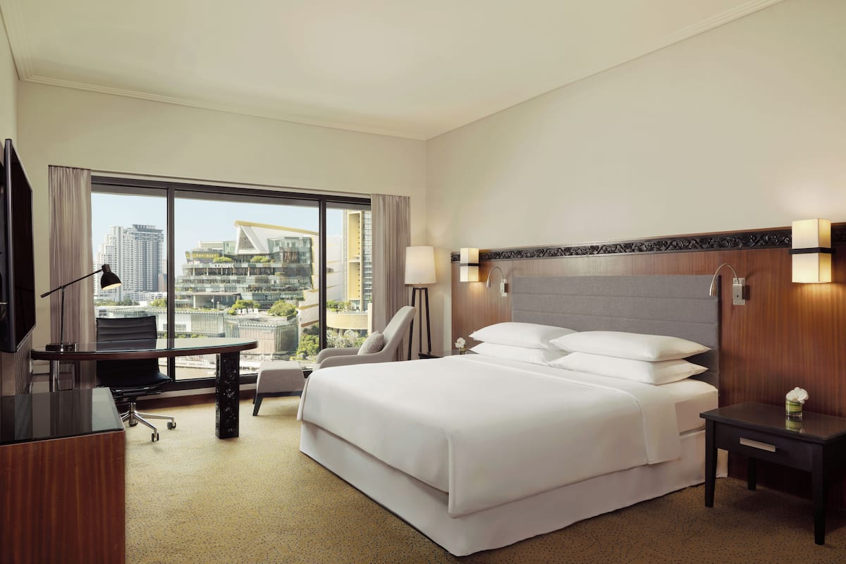 Habitación de hotel con una cama grande, un escritorio, una silla, un televisor y vistas a la ciudad.