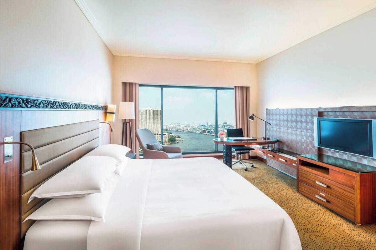 Habitación de hotel con una cama grande, un escritorio con una computadora portátil, un televisor de pantalla plana y vistas a la ciudad.