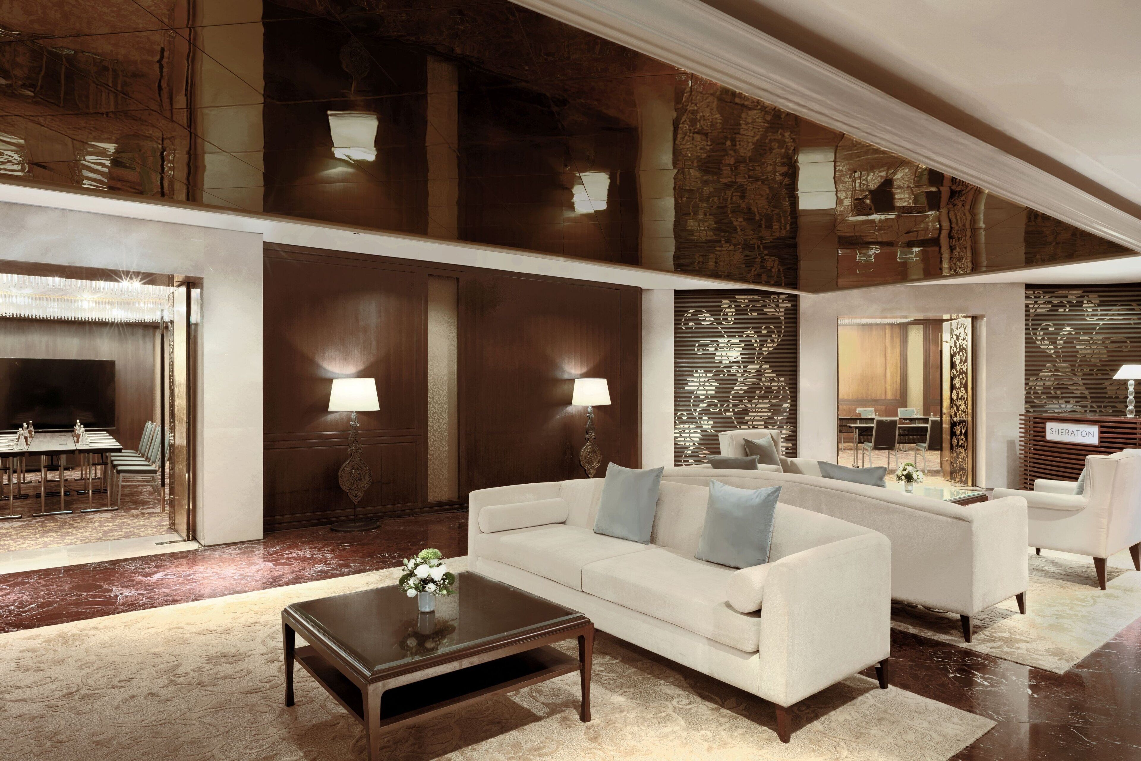 A spacious lobby with a white sofa, a coffee table, and a dining area visible through a glass partition.
