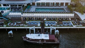 A modern hotel with a pool, outdoor seating, and a boat docked at the entrance. - Royal Orchid Sheraton Riverside Hotel Bangkok (Bangkok)