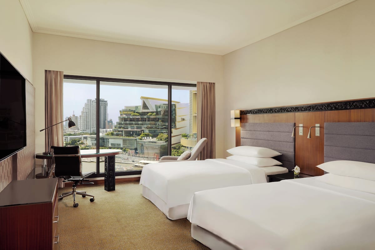 Habitación de hotel con dos camas, un escritorio, una silla, un televisor y un ventanal con vistas a la ciudad.