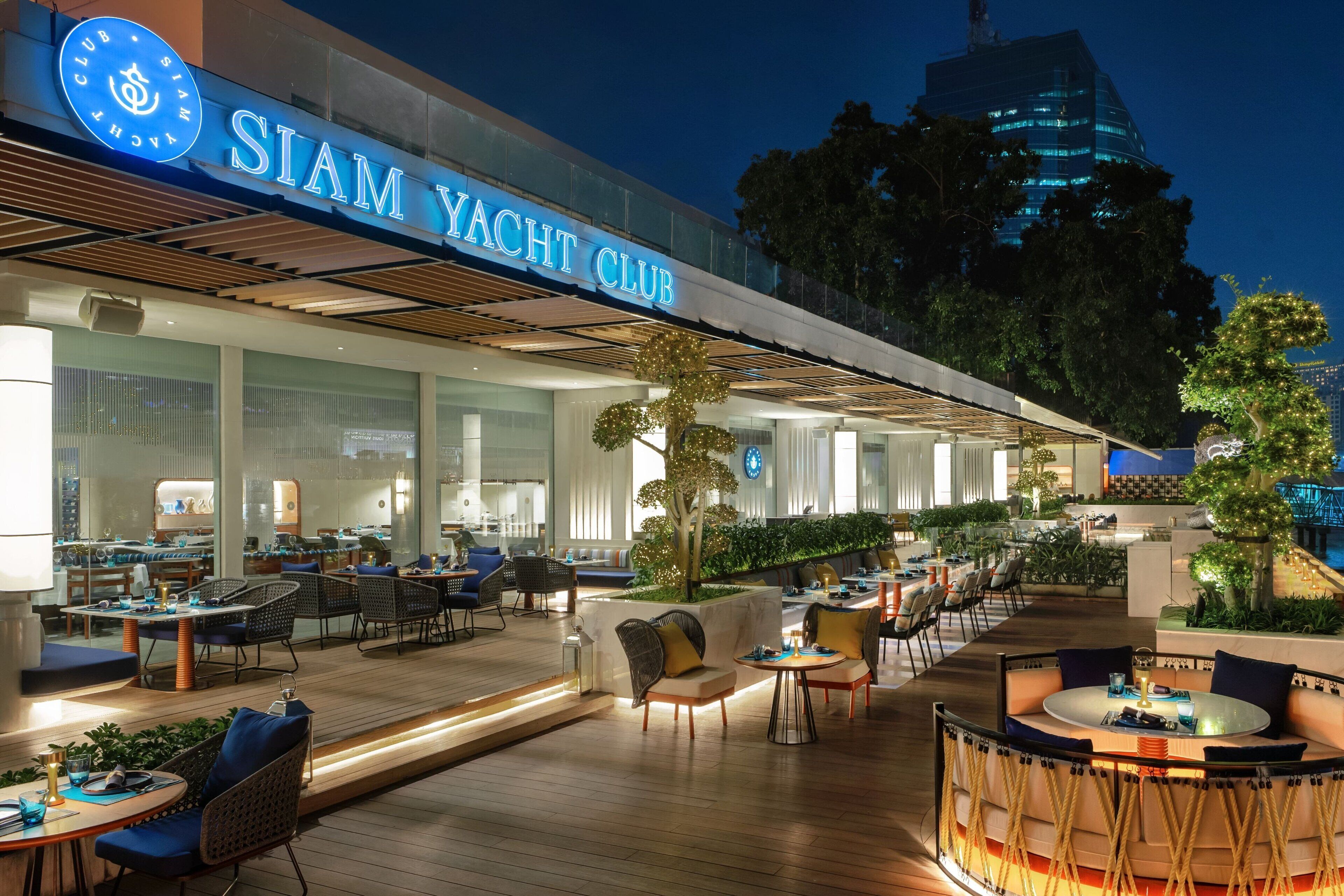 A modern yacht club with outdoor seating and a well-lit facade.