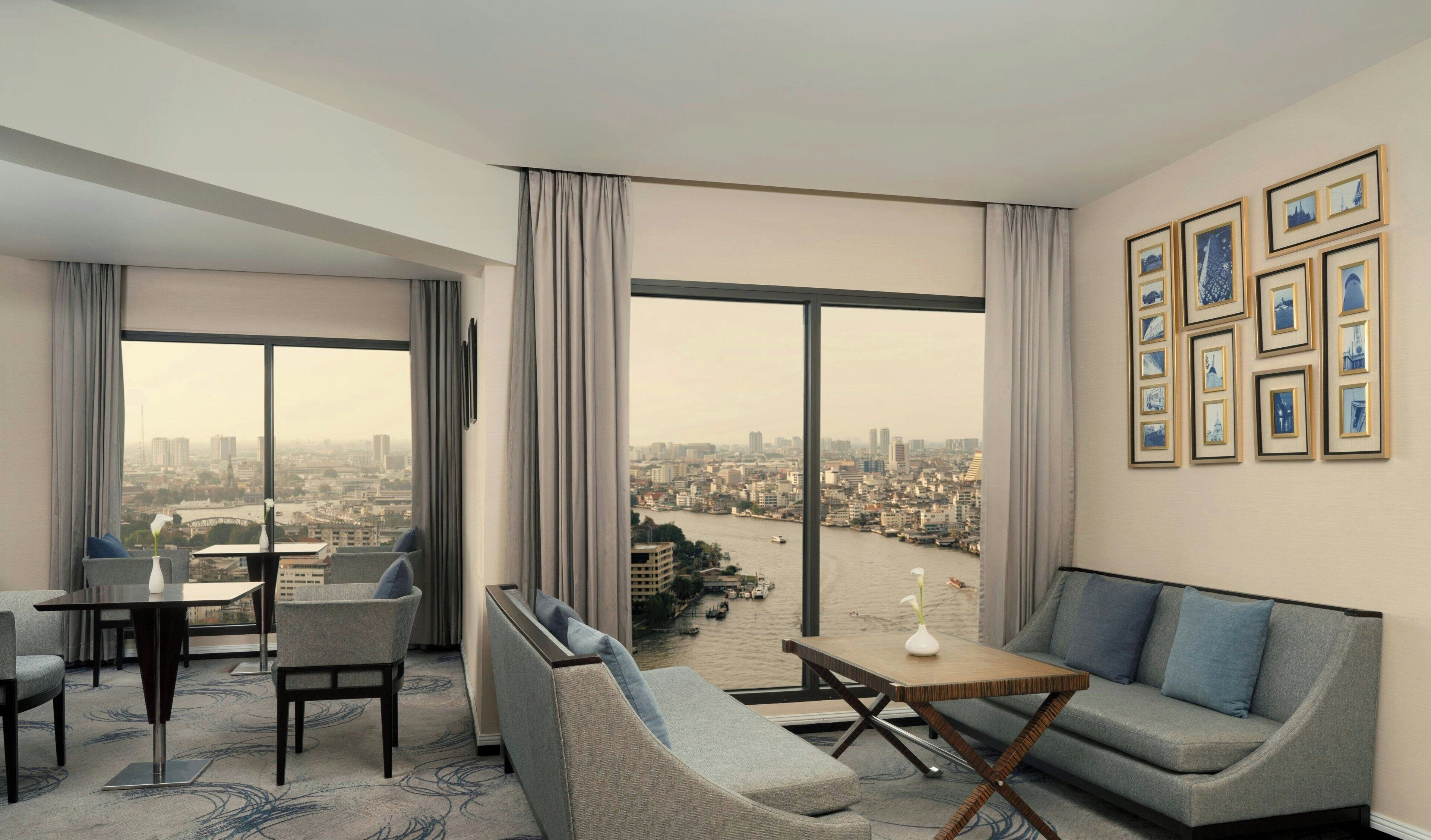 A modern hotel room with a city view, a dining area, and a seating area with a sofa and chairs.