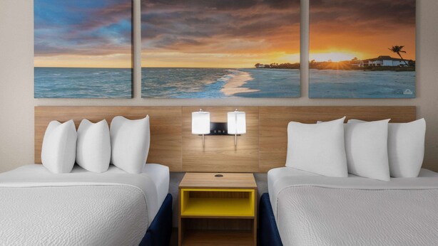 A hotel room with two beds, a wooden headboard, a nightstand, and three sunset paintings on the wall. - Days Inn by Wyndham Florence Near Civic Center (Florence)