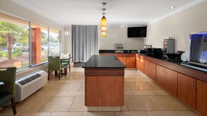 A modern kitchen with a central island, a dining area with chairs, a large window with a view of palm trees, and a flat-screen TV mounted on the wall. - Days Inn by Wyndham Florence Near Civic Center (Florence)