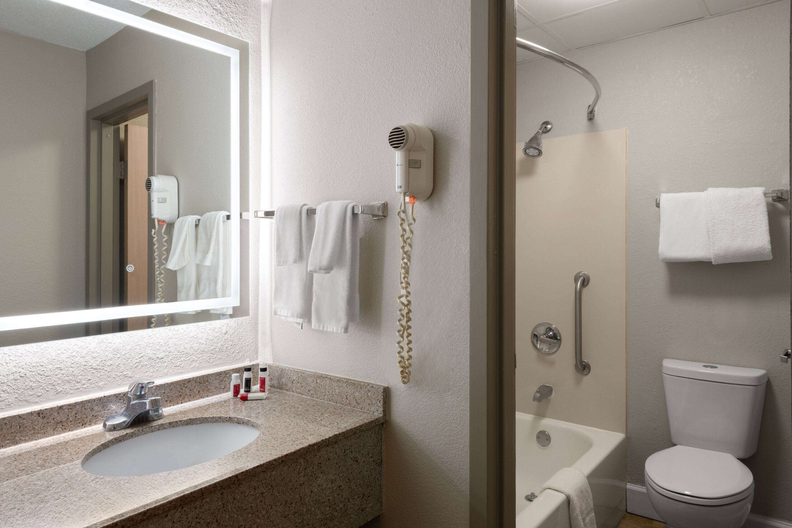 A bathroom with a sink, mirror, hair dryer, and shower.