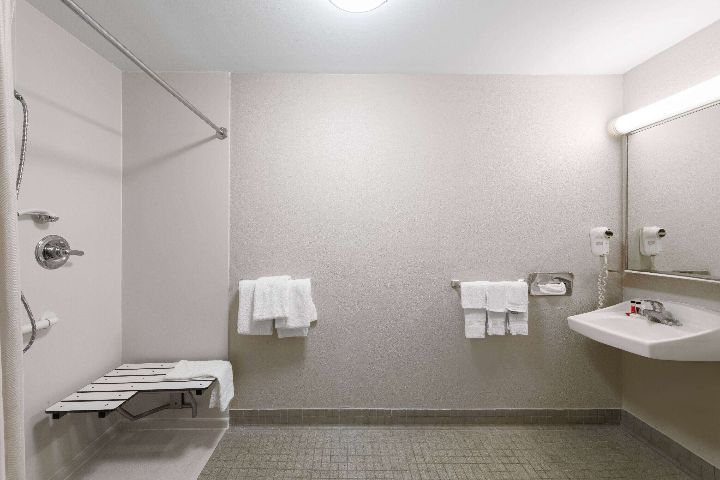 Une salle de bain moderne avec une douche, un banc, un lavabo et des serviettes accrochées au mur.