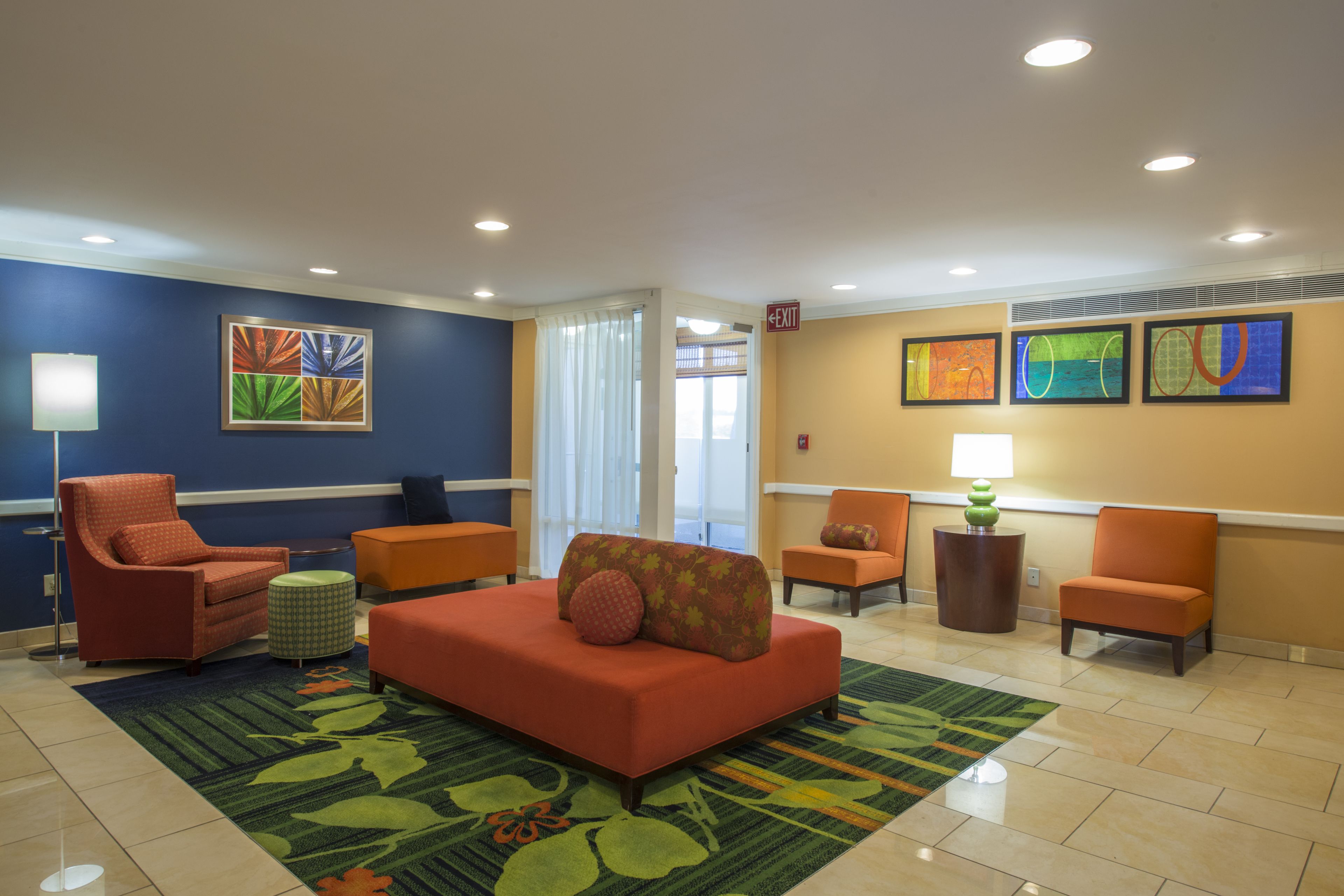 Un hall d’entrée avec un canapé rouge, des fauteuils orange, un tapis à motifs verts et des œuvres d’art accrochées aux murs.