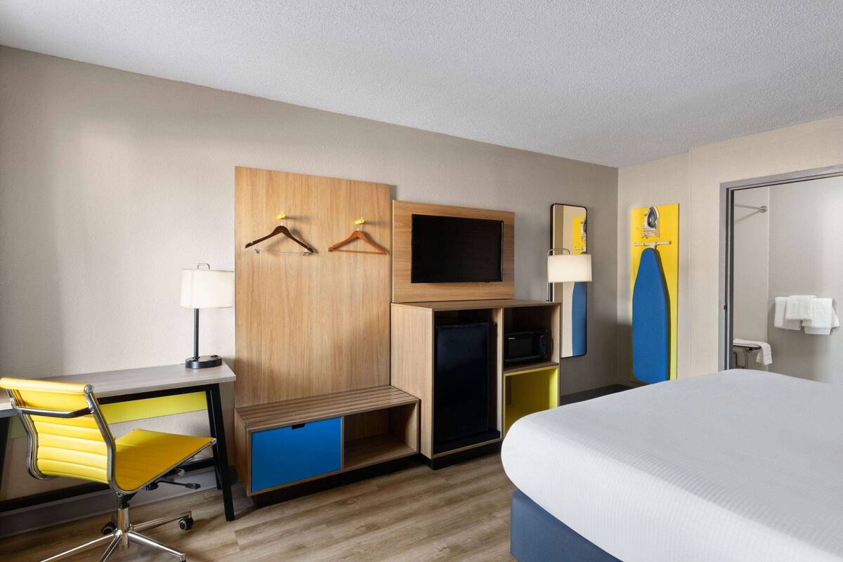 A hotel room with a bed, a desk with a chair, a television, a wardrobe, and a bathroom.