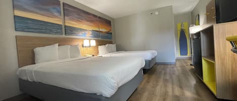 A hotel room with two beds, a wooden headboard, a wall-mounted TV, and a small kitchenette.