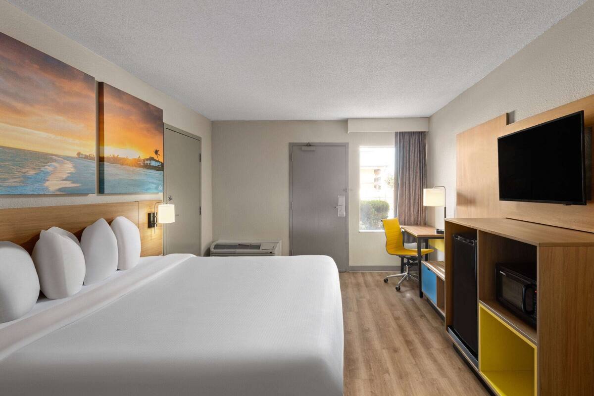 A hotel room with a large bed, a desk with a chair, a flat-screen TV, and a painting on the wall.