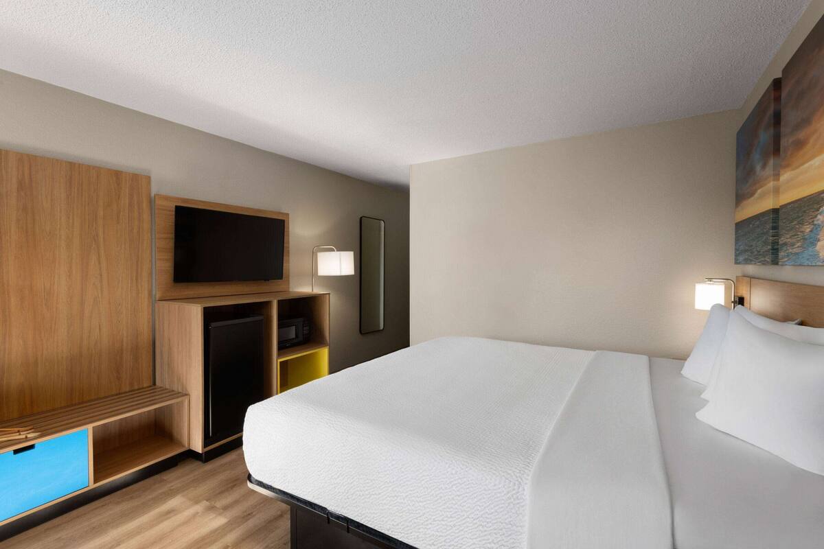 A hotel room with a bed, a TV, a desk with a lamp, and a painting on the wall.