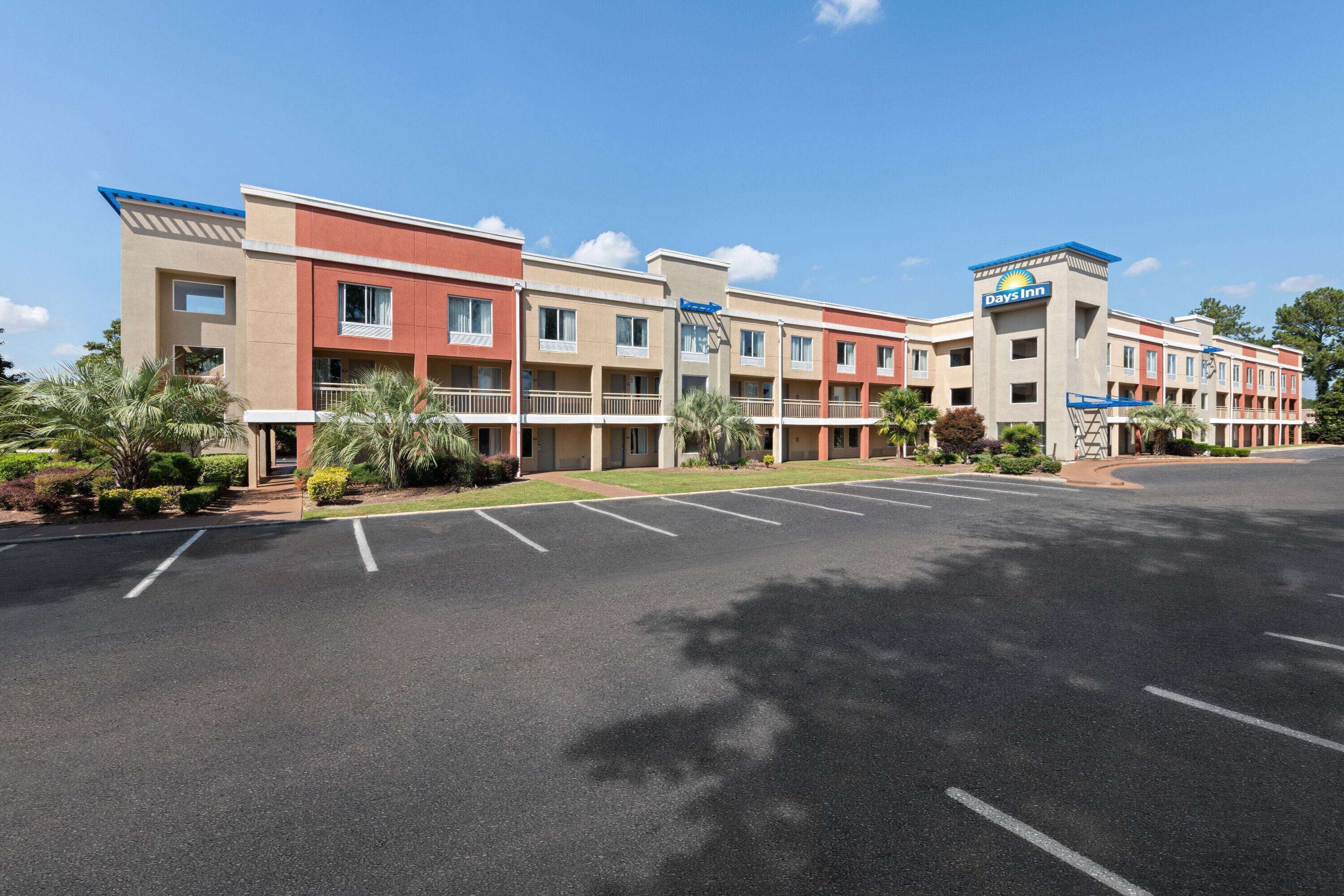 A multi-story hotel with a flat roof and a parking lot in front.