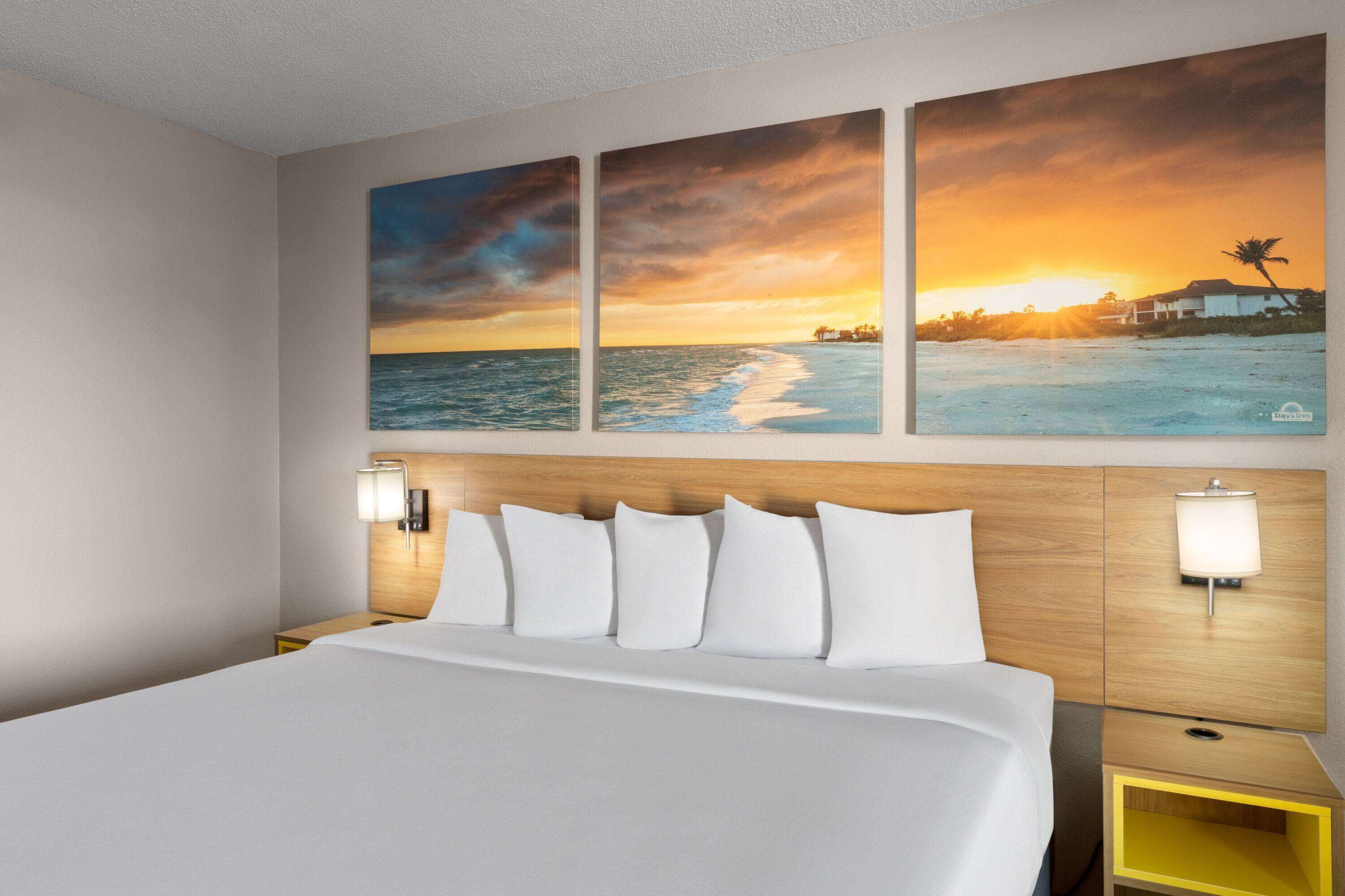 Habitación de hotel con una cama grande, dos mesitas de noche y una obra de arte en la pared que representa un atardecer sobre el océano.