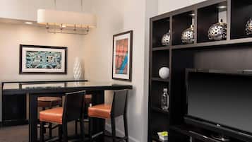 Une chambre d’hôtel moderne avec un coin bar, deux tabourets de bar, un téléviseur à écran plat et des vases décoratifs disposés sur des étagères.