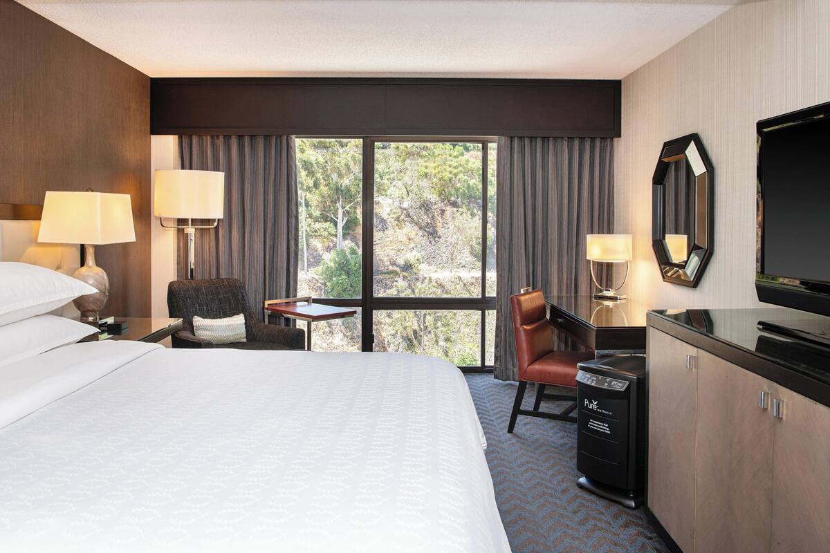 Une chambre d’hôtel avec un grand lit, un bureau, une chaise, une télévision et un mini-bar.