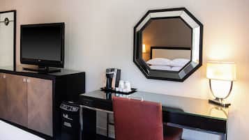 A hotel room with a bed, a desk with a computer, a television, a coffee maker, and a mirror.