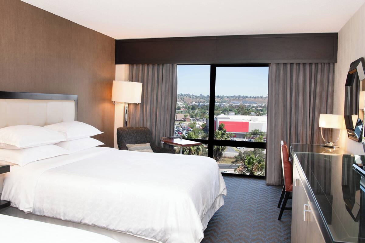 Une chambre d’hôtel avec un grand lit, un bureau et une vue sur le paysage urbain.