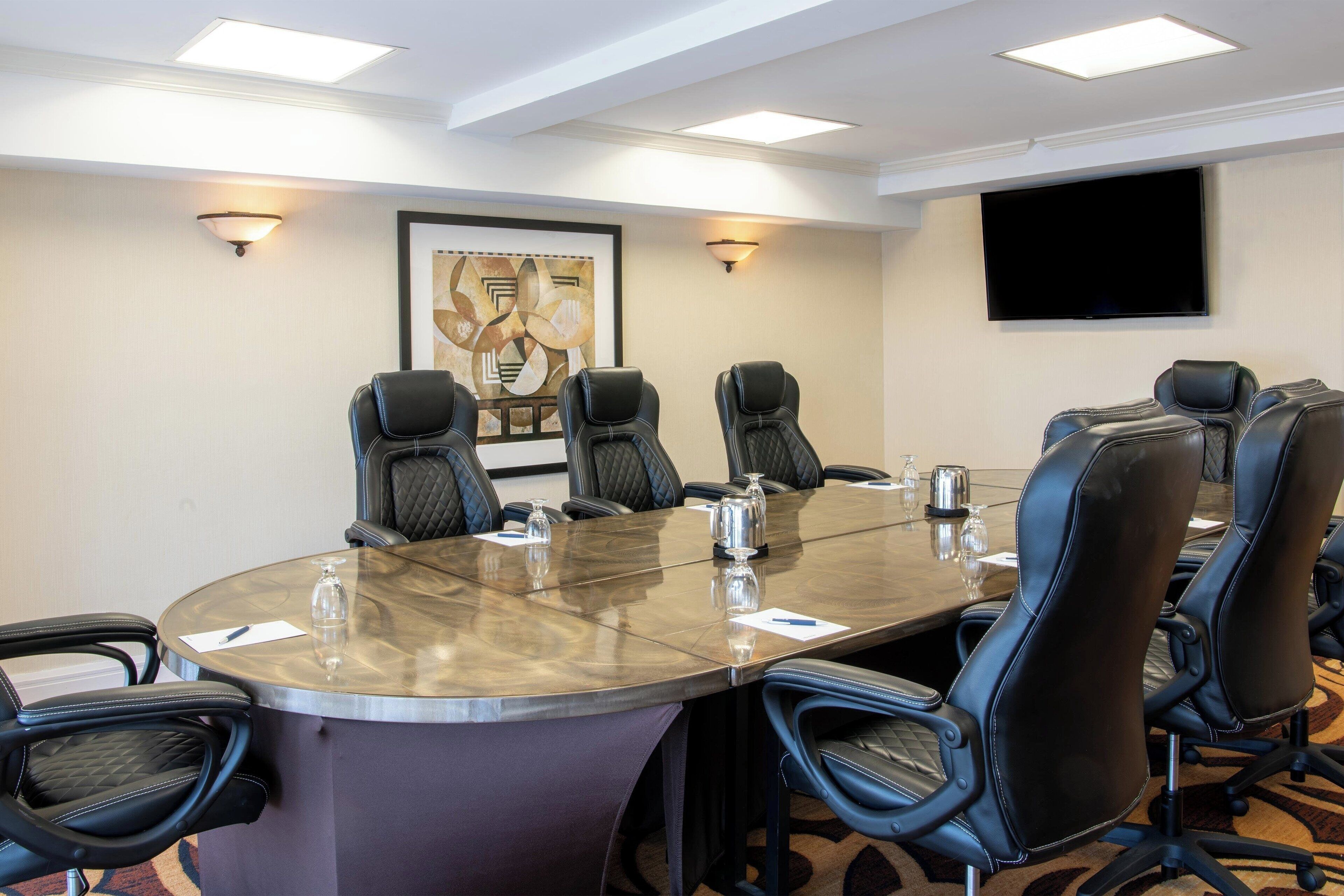 A conference room with a round table, black leather chairs, a flat-screen TV, and wall-mounted lights.