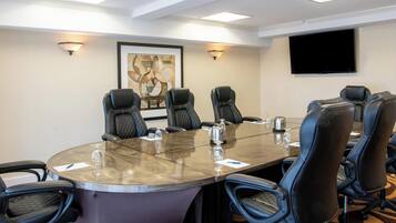 A conference room with a round table, black leather chairs, a flat-screen TV, and wall-mounted lights.