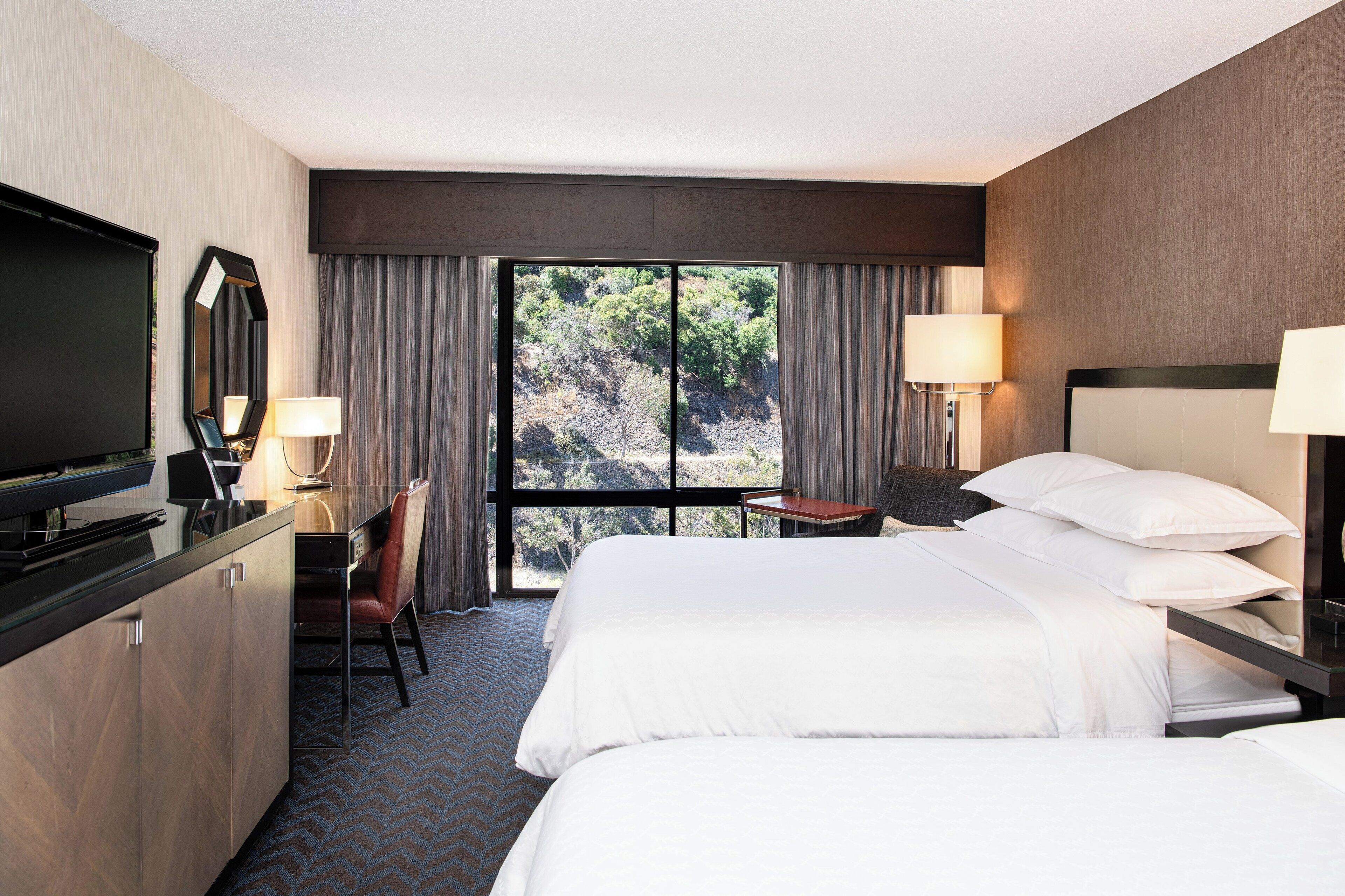 A hotel room with a bed, a desk, a chair, a TV, and a window with curtains.