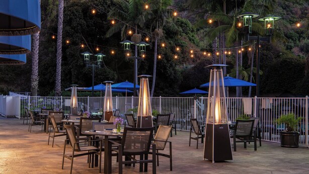 Een terras buiten met tafels, stoelen, lichtslingers en parasols.