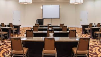 Una sala de conferencias con una pantalla grande, varias mesas y sillas.