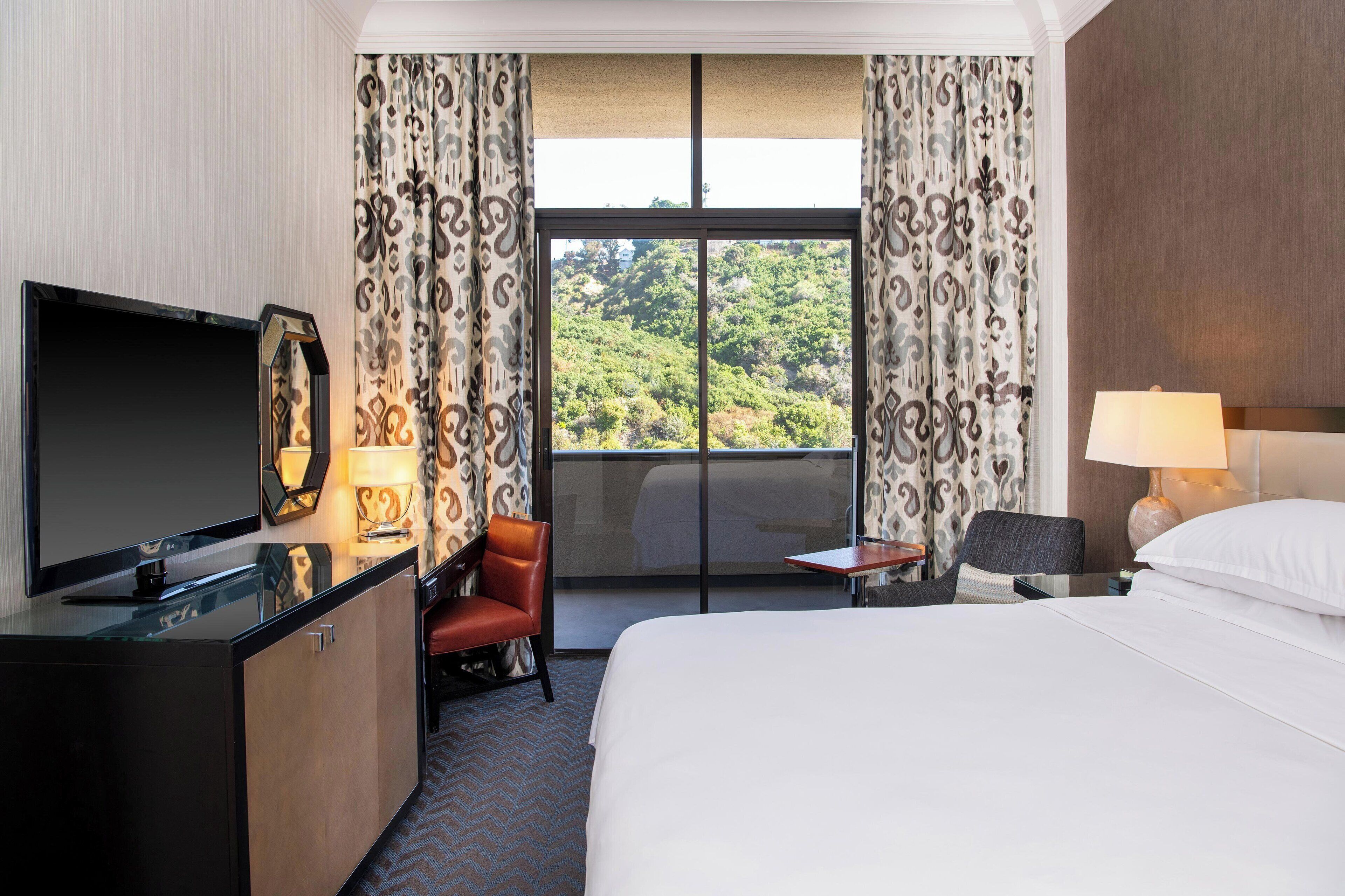 Ein Hotelzimmer mit Bett, Schreibtisch, Flachbildfernseher, Sessel, kleinem Tisch und Lampe.
