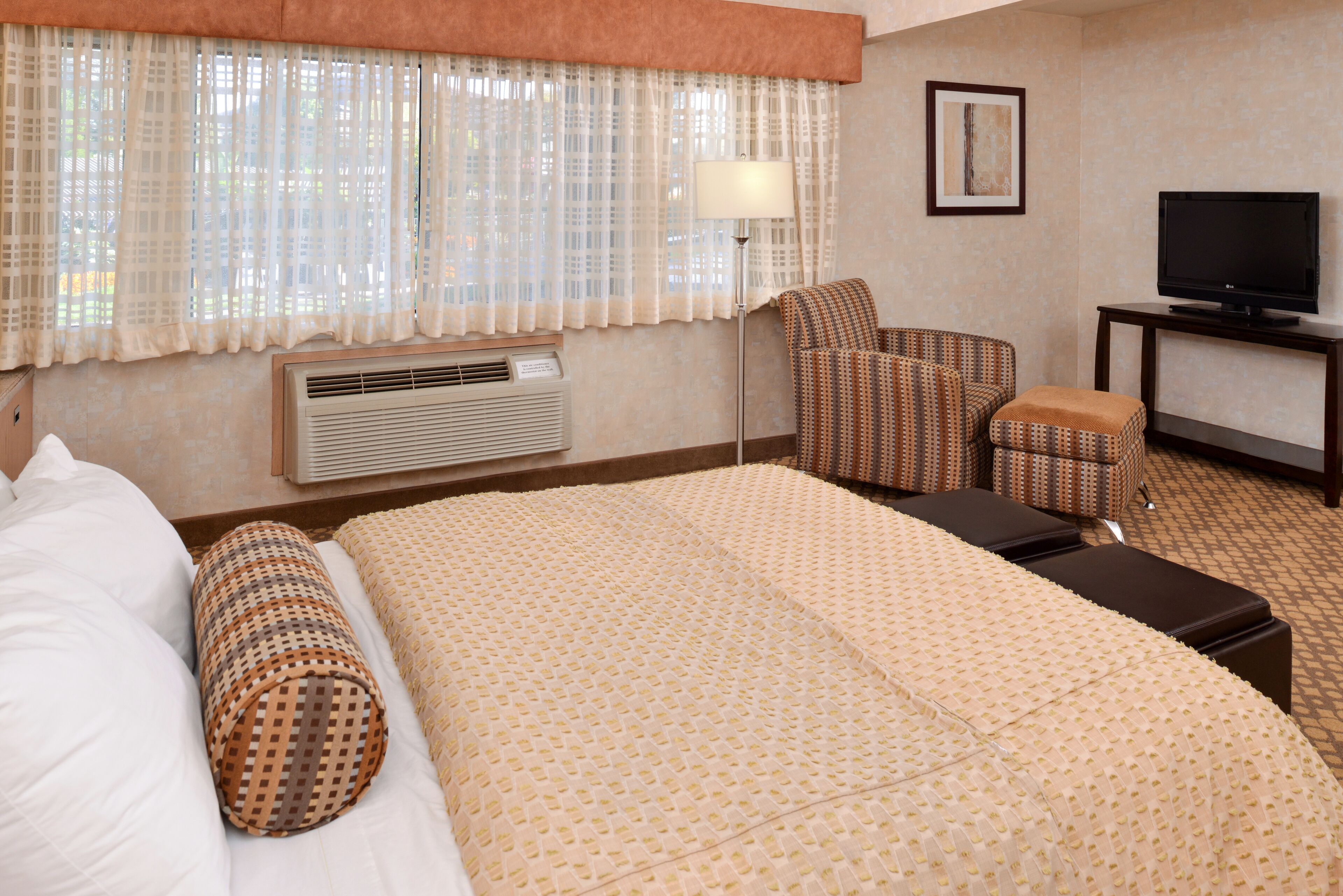 A hotel room with a large bed, a chair, a television, and a lamp.