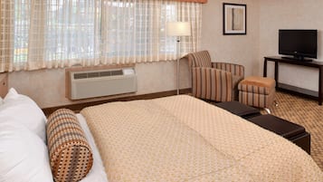 Quarto de hotel com uma cama grande, uma cadeira, uma televisão e uma luminária.