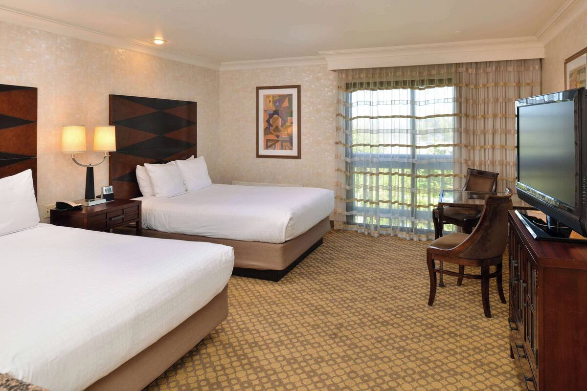 A hotel room with two beds, a desk with a chair, a television, and a window with curtains.