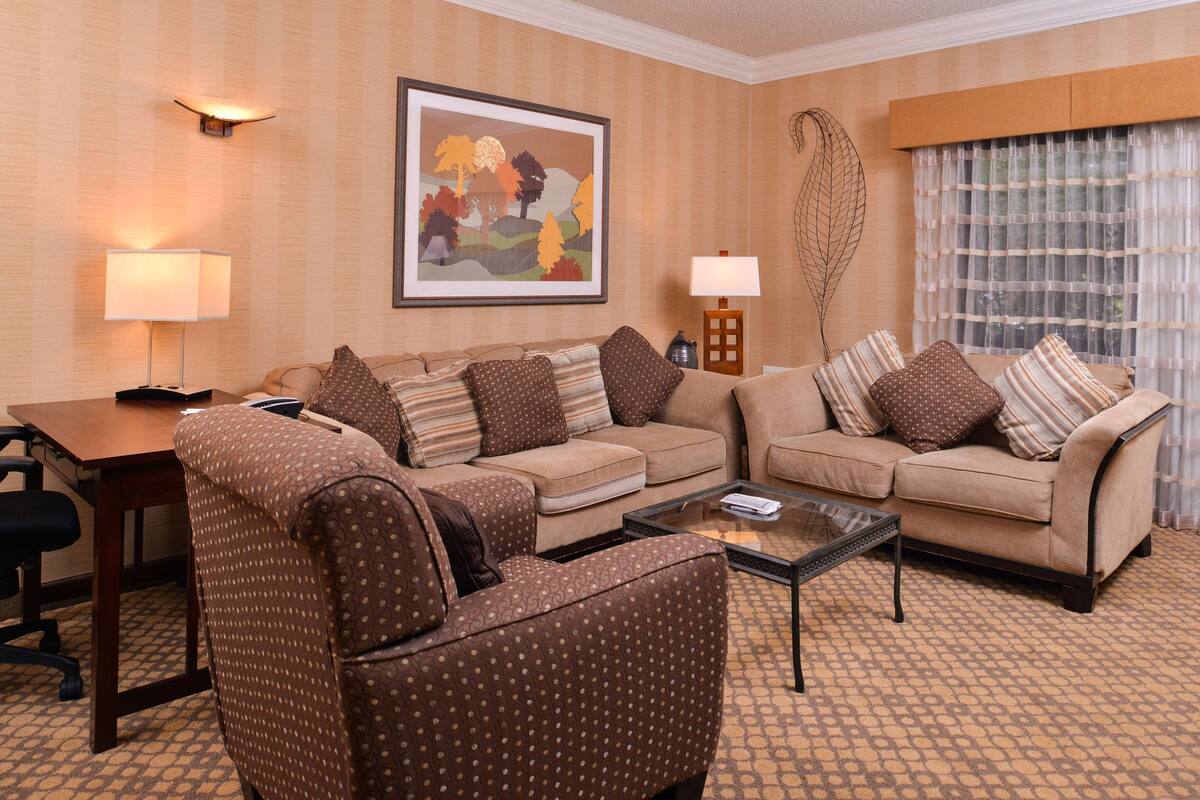 A hotel room with a sofa set, a coffee table, a desk, and a lamp.